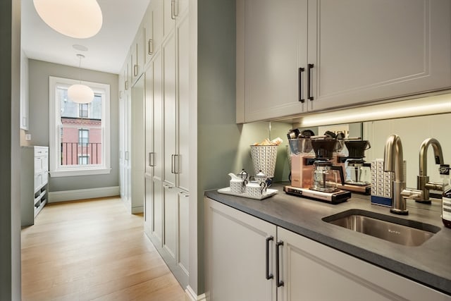 bar featuring white cabinets, light hardwood / wood-style floors, hanging light fixtures, and sink