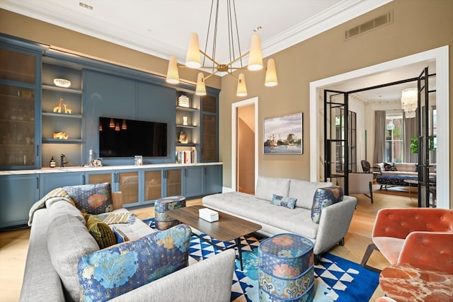 living room with light hardwood / wood-style flooring, a chandelier, crown molding, and built in features