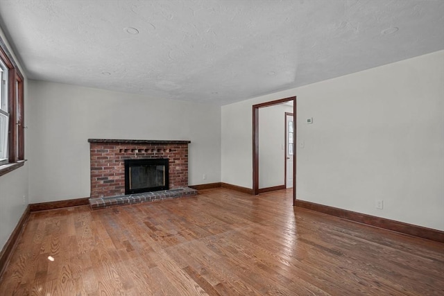 unfurnished living room featuring a fireplace, a textured ceiling, baseboards, and wood finished floors