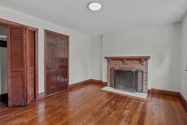 unfurnished living room featuring a brick fireplace, baseboards, and wood-type flooring