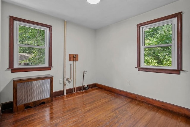 unfurnished room featuring baseboards, wood finished floors, and radiator heating unit