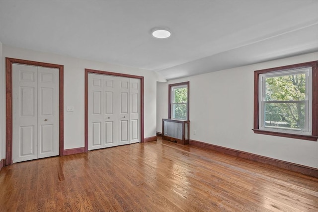 unfurnished bedroom with a closet, radiator heating unit, baseboards, and wood finished floors