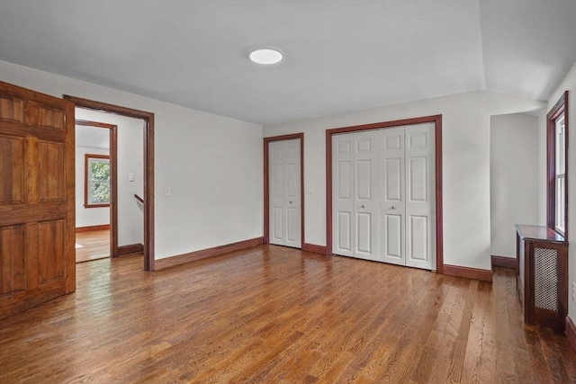 unfurnished bedroom with two closets, baseboards, and wood finished floors