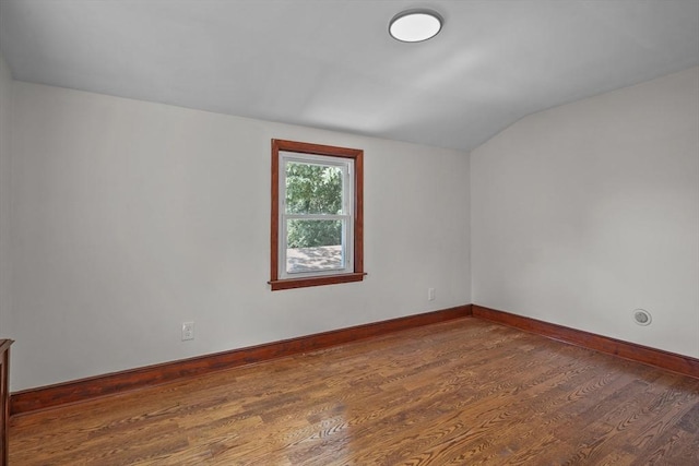 empty room featuring baseboards, lofted ceiling, and wood finished floors