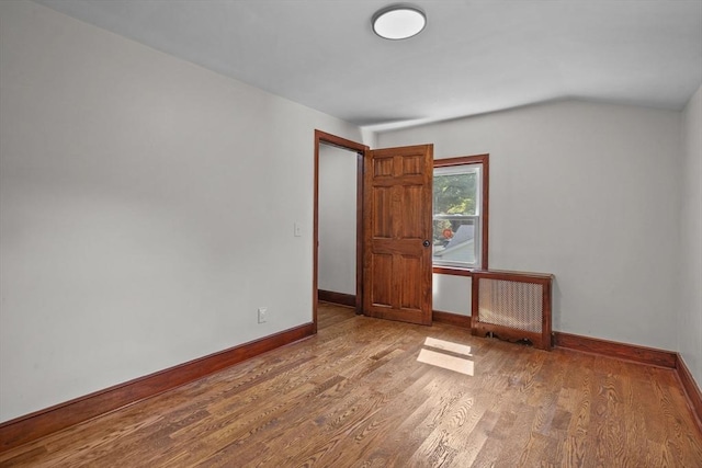 spare room featuring vaulted ceiling, wood finished floors, and baseboards