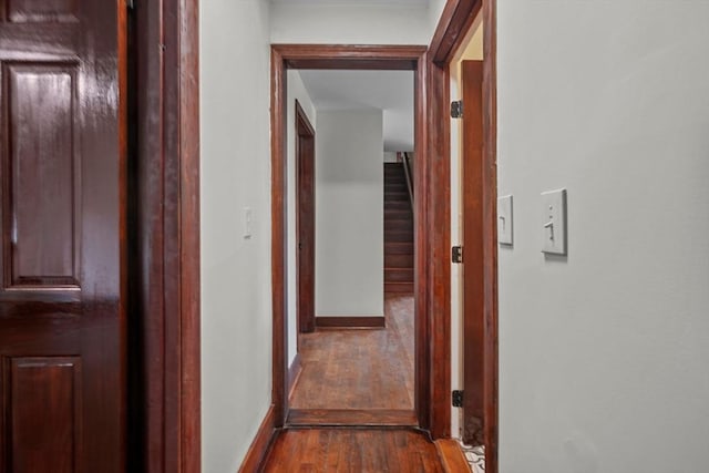 corridor featuring dark wood finished floors, stairway, and baseboards