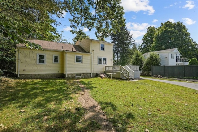 rear view of house with a lawn, a deck, and fence