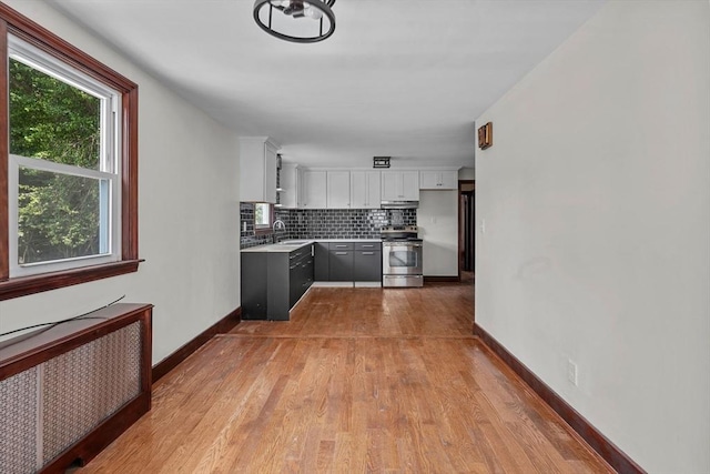 kitchen featuring electric stove, a sink, radiator heating unit, white cabinets, and decorative backsplash