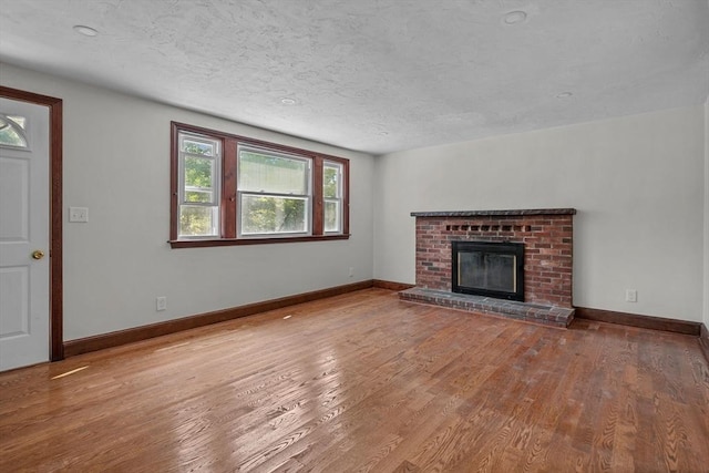 unfurnished living room with a fireplace, a textured ceiling, baseboards, and wood finished floors