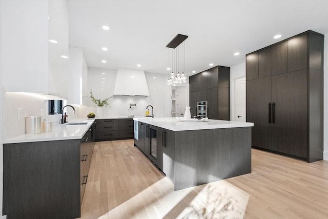 kitchen featuring an island with sink, light wood-type flooring, decorative light fixtures, and custom exhaust hood