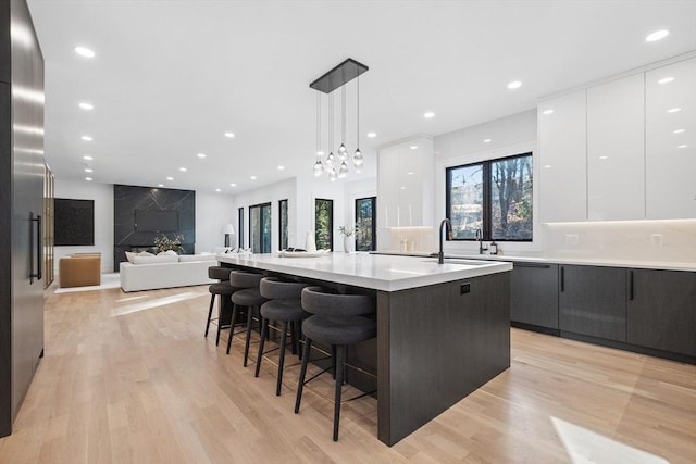 kitchen featuring pendant lighting, a kitchen island with sink, white cabinets, a kitchen breakfast bar, and light hardwood / wood-style floors