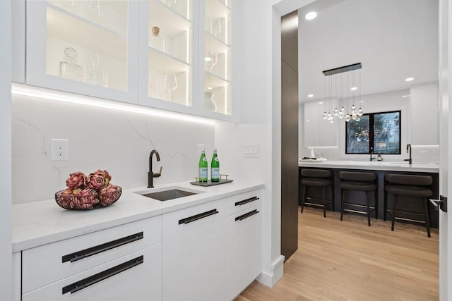 bar with decorative backsplash, sink, white cabinets, and light wood-type flooring