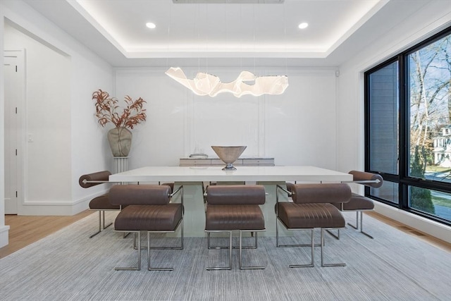 dining space with a raised ceiling and light wood-type flooring