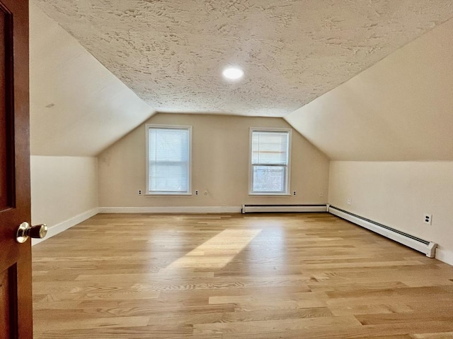 additional living space featuring lofted ceiling, light wood-type flooring, and a baseboard heating unit