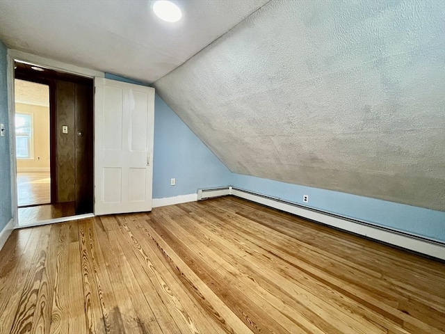 bonus room featuring vaulted ceiling, a baseboard radiator, light hardwood / wood-style floors, and a textured ceiling