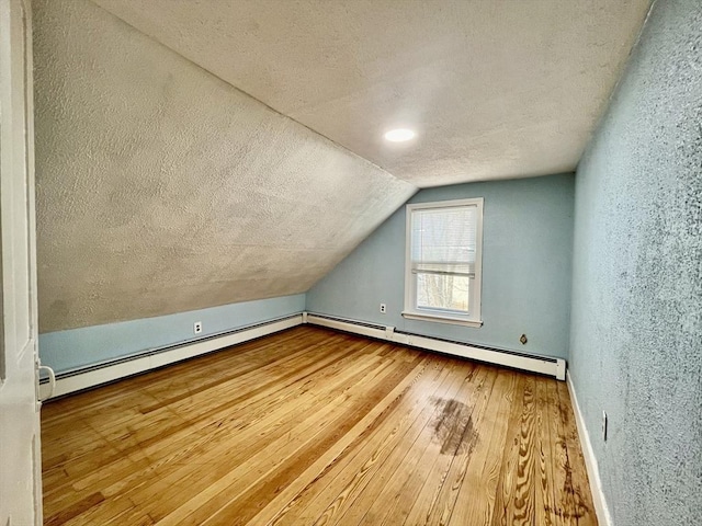 additional living space featuring a textured ceiling, wood-type flooring, vaulted ceiling, and a baseboard heating unit