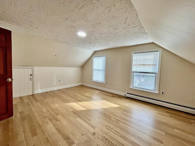 additional living space featuring a textured ceiling, light hardwood / wood-style flooring, a baseboard radiator, and vaulted ceiling