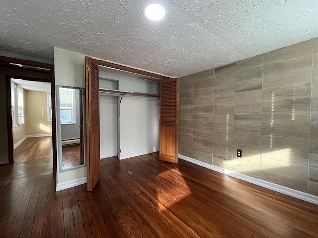 unfurnished bedroom featuring a textured ceiling, a closet, dark hardwood / wood-style floors, and a baseboard heating unit