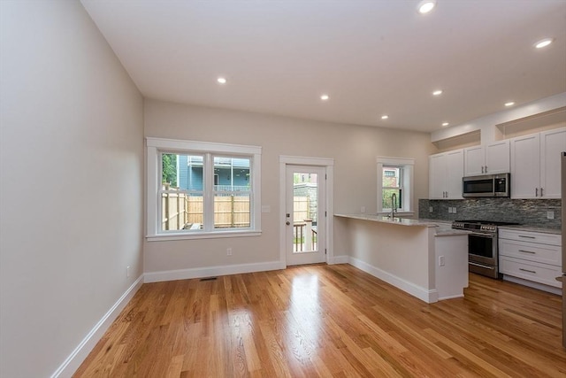 kitchen featuring white cabinetry, backsplash, kitchen peninsula, stainless steel appliances, and light hardwood / wood-style flooring