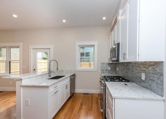 kitchen featuring sink, white cabinetry, appliances with stainless steel finishes, a kitchen breakfast bar, and light stone countertops