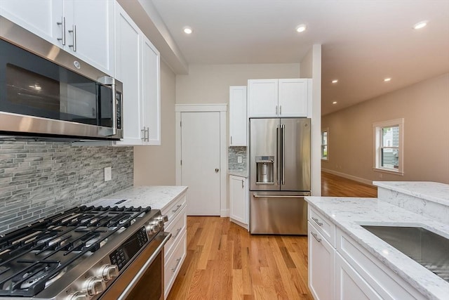 kitchen with appliances with stainless steel finishes, white cabinetry, backsplash, light stone counters, and light wood-type flooring