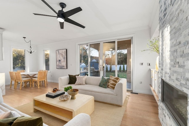 living room with ornamental molding, ceiling fan with notable chandelier, light hardwood / wood-style floors, and a fireplace