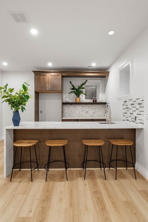 bar with sink, light wood-type flooring, and decorative backsplash