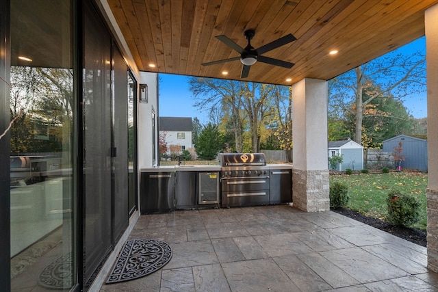 patio terrace at dusk featuring a grill, a lawn, exterior kitchen, ceiling fan, and a storage shed