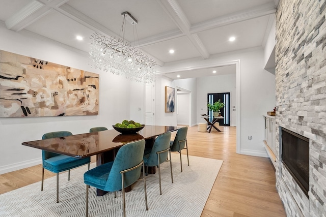 dining space with a stone fireplace, light wood-type flooring, and beamed ceiling