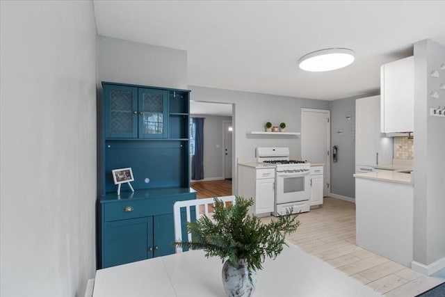 kitchen with white cabinets, light countertops, white gas stove, light wood-style floors, and open shelves