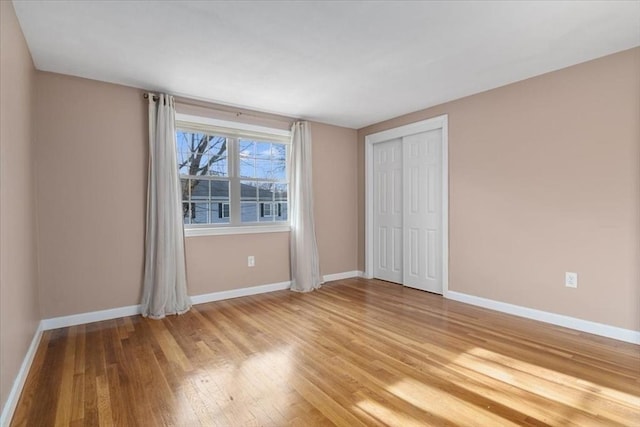 unfurnished bedroom featuring light wood-style floors, baseboards, and a closet