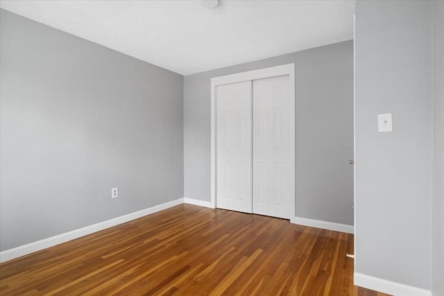 unfurnished bedroom with a closet, wood finished floors, and baseboards