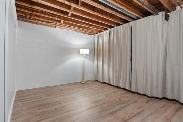 unfinished below grade area featuring light wood-type flooring and concrete block wall