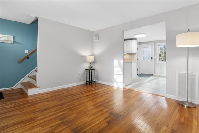 unfurnished living room with light wood-style flooring, stairs, visible vents, and baseboards