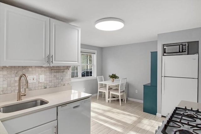 kitchen with light countertops, backsplash, white cabinets, a sink, and white appliances