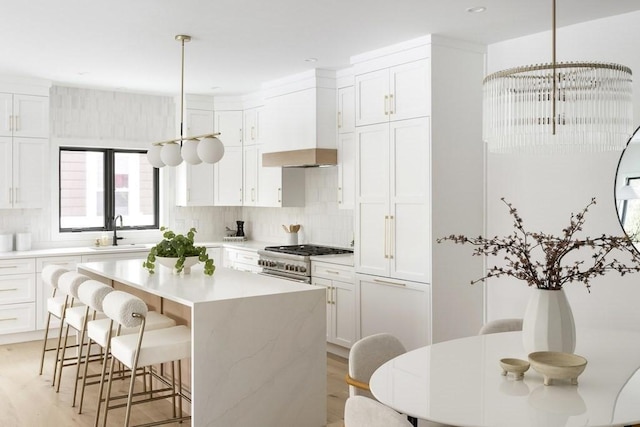 224 Auburn St Unit F, Newton, MA 02466 - kitchen with a chandelier, tasteful backsplash, stainless steel stove, white cabinets, and wall chimney exhaust hood
