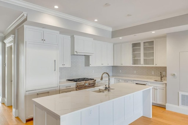 kitchen featuring stainless steel stove, sink, white cabinets, a kitchen island with sink, and light stone counters