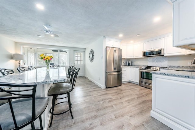 kitchen with light stone countertops, appliances with stainless steel finishes, light wood-style flooring, and white cabinetry