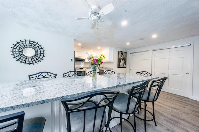 kitchen with a kitchen bar, light wood finished floors, appliances with stainless steel finishes, and white cabinetry