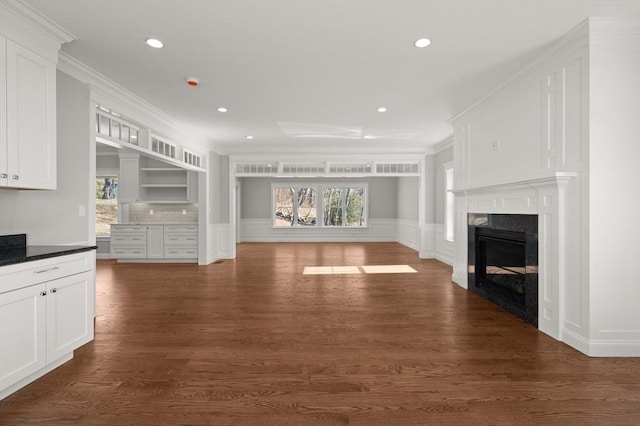 unfurnished living room with dark wood finished floors, a wainscoted wall, crown molding, a fireplace, and a decorative wall