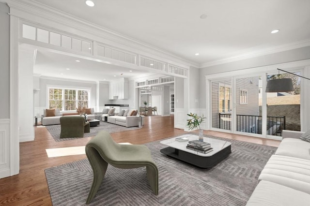 living room featuring ornamental molding, a decorative wall, wood finished floors, and wainscoting