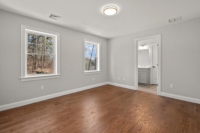 unfurnished bedroom featuring baseboards, connected bathroom, visible vents, and wood finished floors