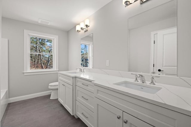 bathroom featuring double vanity, a sink, toilet, and baseboards