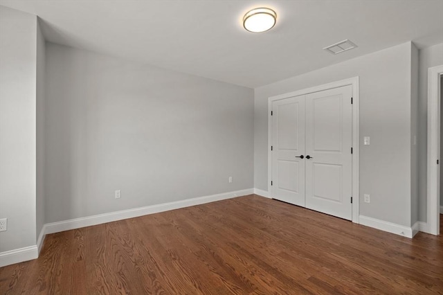 unfurnished bedroom featuring visible vents, a closet, baseboards, and wood finished floors