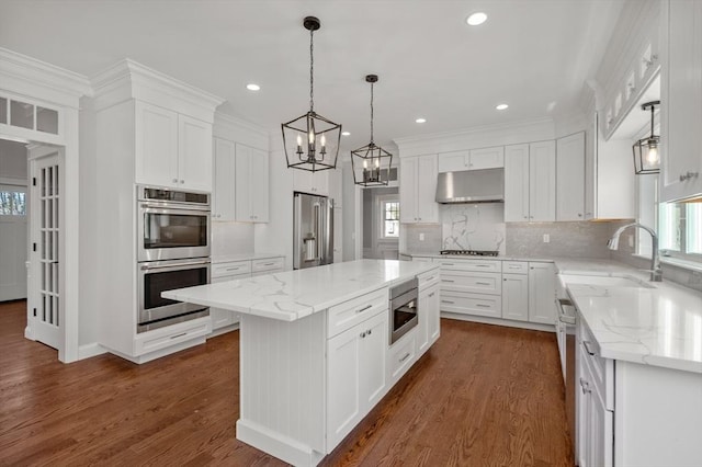 kitchen with white cabinets, a kitchen island, appliances with stainless steel finishes, under cabinet range hood, and a sink