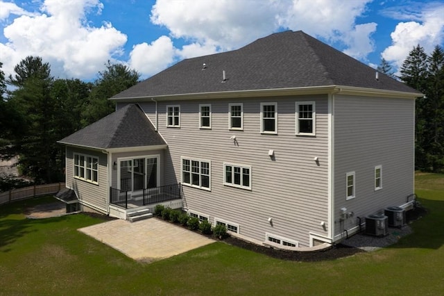 rear view of house featuring a patio, a shingled roof, and a lawn