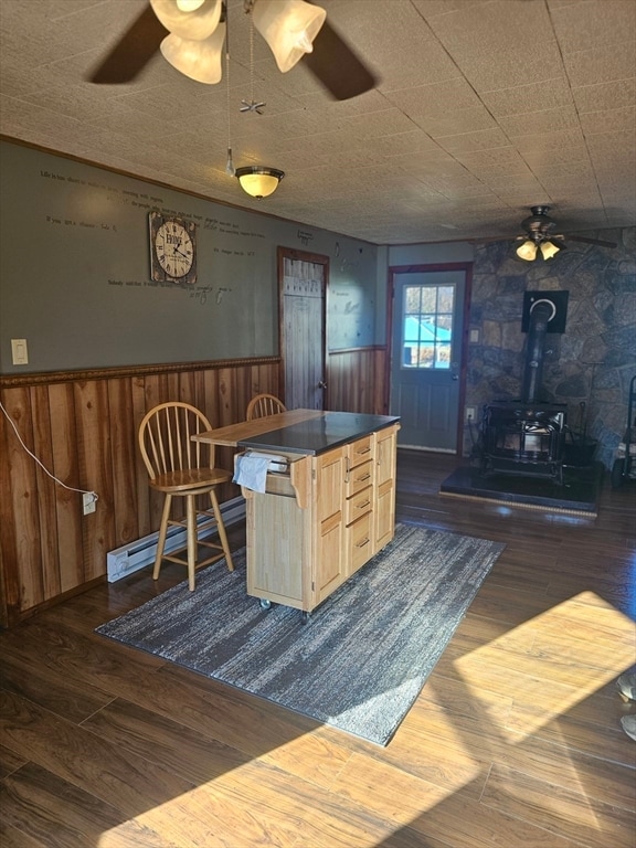 dining area with a wood stove, dark wood-type flooring, and wooden walls