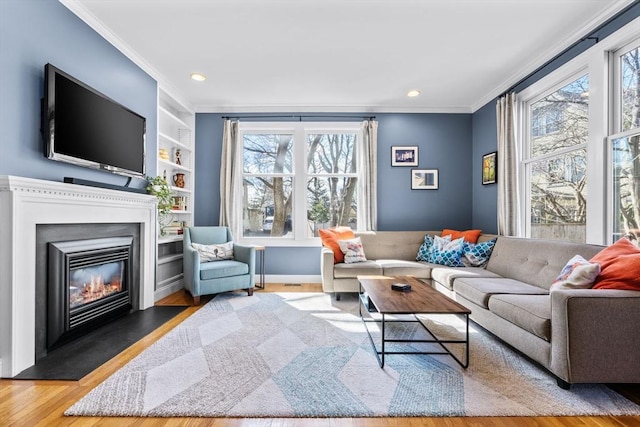 living area featuring built in features, wood finished floors, recessed lighting, ornamental molding, and a glass covered fireplace
