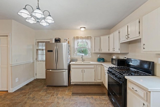 kitchen with freestanding refrigerator, black gas range oven, a sink, light countertops, and a chandelier