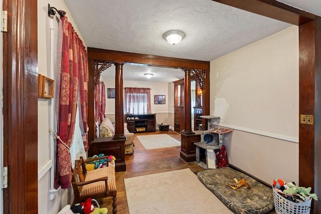 hallway featuring ornate columns, wood finished floors, and a textured ceiling